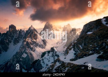 Vue arrière d'un touriste méconnaissable en vêtements de dessus debout sur la neige et observant les pics de Tre cime di Lavaredo contre ciel nuageux ensoleillé dans les Dolomites, il Banque D'Images