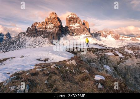 Vue arrière d'un touriste méconnaissable en vêtements de dessus debout sur la neige et observant les pics de Tre cime di Lavaredo contre ciel nuageux ensoleillé dans les Dolomites, il Banque D'Images