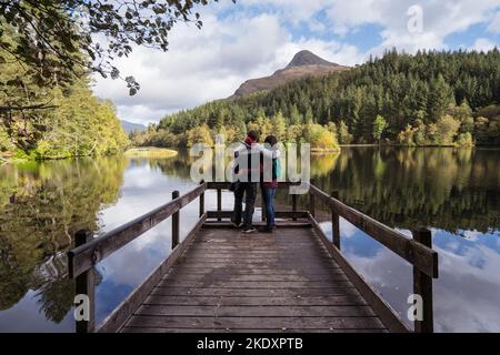 Vue arrière d'une petite amie et d'un petit ami multiracial méconnaissable en vêtements d'extérieur se tenant sur la jetée près du lac réfléchissant contre M. Banque D'Images
