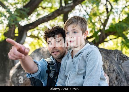 Fils assis sur le tronc d'arbre près d'un père optimiste et regardant loin tout en passant une journée de week-end dans le parc ensemble Banque D'Images