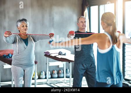 La forme vivante aide à garder leurs fonctions physiques en contrôle. Un homme et une femme âgés utilisant des bandes de résistance avec l'aide d'un thérapeute physique. Banque D'Images