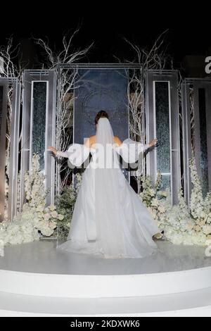 Une mariée luxueuse dans une belle robe se tient avec elle dos à l'arche de mariage avant la cérémonie de soirée Banque D'Images