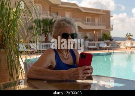 Crète Grèce.2022. Femme âgée utilisant un téléphone portable près de la piscine de l'hôtel. Banque D'Images