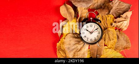 Horloge sur les feuilles d'automne jaunes avec fond de bannière rouge. Banque D'Images