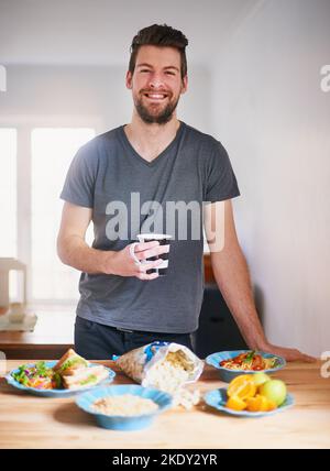 Remplir mon alimentation avec des aliments sains et nutritifs. Portrait d'un beau jeune homme debout devant les repas qu'il a préparés dans sa cuisine. Banque D'Images