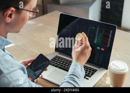 Gros plan sur un homme qui a réussi à négocier ou à négocier un crypto-monnaie en or, assis à une table de bureau avec un ordinateur portable, en investissant dans btc, en utilisant l'application crypto-monnaie Banque D'Images