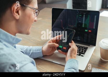 Gros plan d'un professionnel professionnel de crypto expérimenté souriant regardant les cartes relevées de l'application de marché de crypto sur les écrans d'ordinateur portable et de téléphone dans les mains, décider de la météo acheter ou de vendre la monnaie pour réussir Banque D'Images