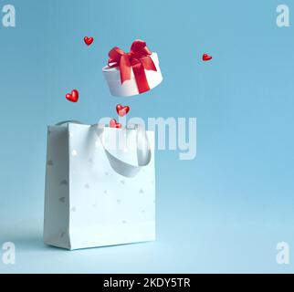 Sac à provisions avec boîte cadeau et coeurs sur fond bleu. Concept de shopping et de réductions pour la Saint-Valentin Banque D'Images