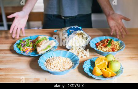 C'est ce que je mange dans une journée. Gros plan d'un homme montrant différents aliments de son régime alimentaire sur une table. Banque D'Images
