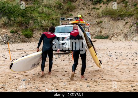 Deux sauveteurs RNLI marchent sur la plage vers leur camion transportant des planches de sauvetage, Fistral Beach, Newquay. Banque D'Images