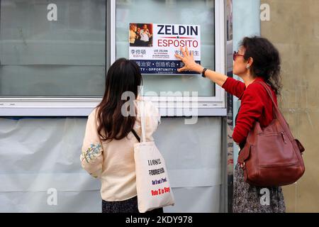 Deux agents de la campagne politique asiatique américaine placent une affiche Zeldin/Esposito sur une fenêtre d'un bâtiment dans le quartier chinois de Manhattan, à 6 novembre 2022. Banque D'Images