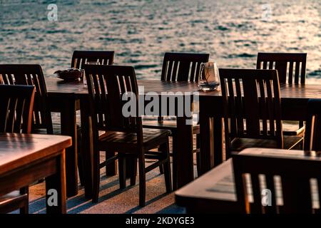 Rangée de tables et chaises en bois d'un restaurant sur la plage de Thaïlande, pas de personnes, coucher de soleil, fond flou de la vague de mer. Banque D'Images