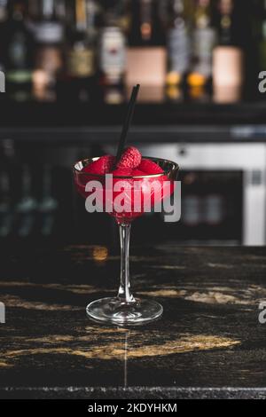 Un gros plan vertical d'un cocktail cosmopolite servi avec une fraise dans un verre dans un café Banque D'Images