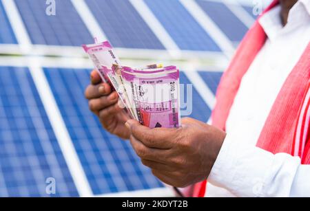gros plan sur les mains des agriculteurs comptant de l'argent devant le panneau solaire - conepte d'économies, de profits et d'investissements dans l'énergie solaire pour l'électricité Banque D'Images