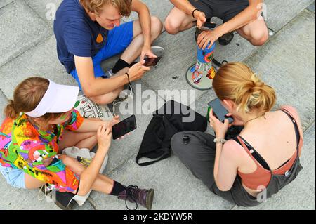 Une photo aérienne d'un groupe d'adolescents utilisant leur smartphone assis sur un trottoir à Turin, Italie Banque D'Images