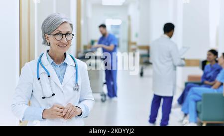 institution médicale. Médecin mûr souriant debout dans le couloir de l'hôpital moderne sur fond d'assistants médicaux et d'infirmières travaillant Banque D'Images
