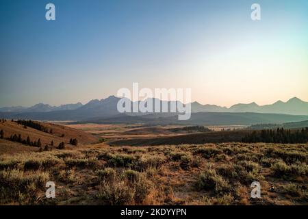 La chaîne de montagnes Sawtooth vue des contreforts au nord de Stanley, Idaho, en soirée d'été. Le ciel est brumeux en raison de la fumée du feu de forêt. Banque D'Images