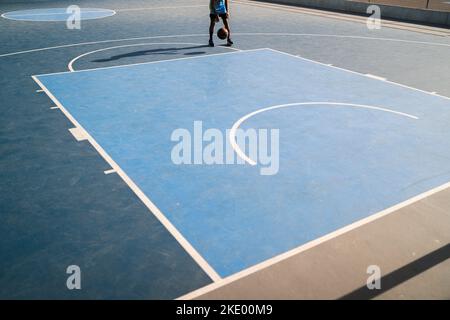 Un enfant jouant au basket-ball sur un terrain de jeu un matin ensoleillé Banque D'Images
