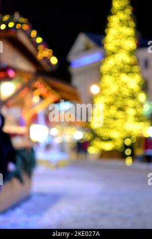 Arrière-plan flou. Noël nouvel an arbre décoré jaune guirlande illuminée, petites maisons en bois guirlande de lanternes sur le toit et silhouettes de personnes marchant le long de la rue de la ville. Banque D'Images