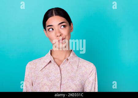 Photo d'une fille malaisienne intelligente et soucieuses regarder l'espace vide intéressé isolé sur fond de couleur cyan vif Banque D'Images