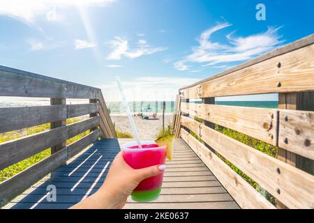 Main tenant un verre avec un cocktail et de la paille sur la plage des rochers indiens en Floride, Etats-Unis Banque D'Images