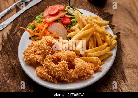 Vue de dessus des crevettes, pommes de terre et légumes frits sur une plaque blanche sur fond de bois Banque D'Images