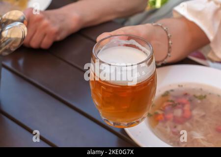 La main d'une femme tient une tasse de bière avec de la mousse blanche dense sur une table en bois. Banque D'Images