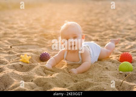 Un petit garçon heureux est couché sur une plage de sable près de la mer, aux rayons du soleil couchant Banque D'Images