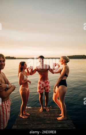 Des amis qui se forment le cœur les uns avec les autres tout en se tenant sur la jetée pendant le coucher du soleil Banque D'Images