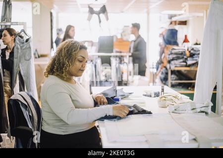 Vue latérale d'une jeune couturier examinant le tissu pendant son travail à l'atelier Banque D'Images