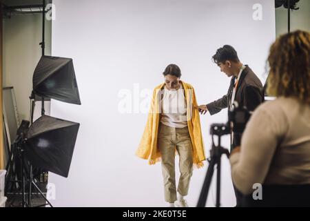 Un designer masculin assiste le mannequin féminin sur fond blanc lors de la prise de photos en studio Banque D'Images