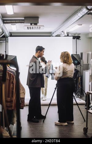 Vue latérale d'un designer de mode masculin assistant le photographe pendant la prise de vue en studio Banque D'Images