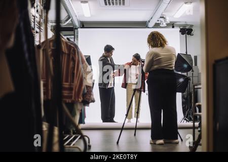 Un professionnel de la conception de sexe masculin assiste le mannequin de mode pendant la prise de vue en studio Banque D'Images