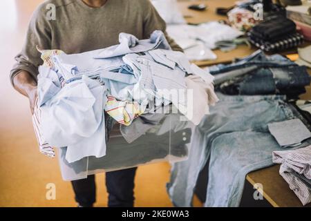 Conception masculine professionnelle tenant des tissus recyclés dans un conteneur à l'atelier Banque D'Images