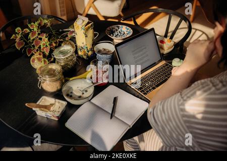 Jeune femme avec ordinateur portable et journal assis à table Banque D'Images