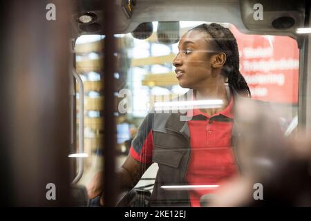 Femme d'entrepôt regardant loin en étant assis dans un chariot élévateur vu par le pare-brise Banque D'Images