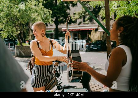 Femme souriante qui cherche à tenir de la guitare au marché aux puces Banque D'Images