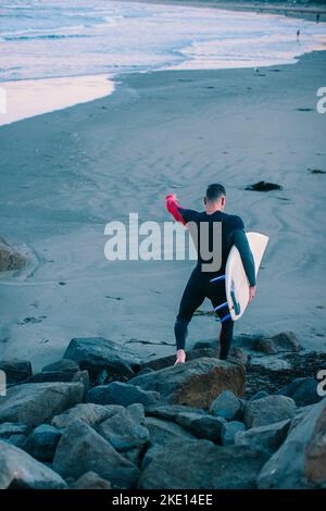 Un homme d'âge moyen saute sur des rochers avec une planche de surf. Banque D'Images