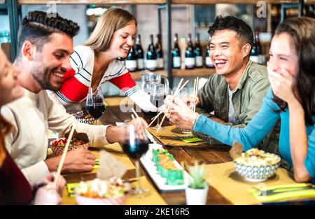 Des amis multiculturels branchés qui mangent des sushis avec des baguettes au bar-restaurant fusion - concept de mode de vie pour les repas et les boissons avec des jeunes heureux Banque D'Images