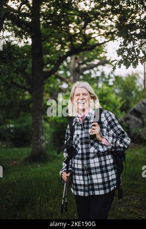 Portrait d'une femme âgée heureuse tenant des bâtons de randonnée tout en faisant de la randonnée en forêt Banque D'Images