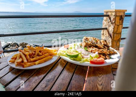 Une assiette de frites et de sardines grillées avec salade, tomate et citron. Restaurant en bordure de la mer Méditerranée avec vue depuis le balcon. Banque D'Images