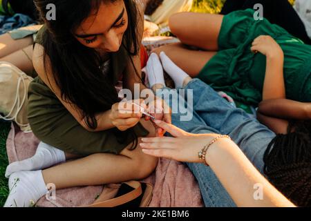 Jeune fille souriante appliquant du vernis à ongles à une amie au parc Banque D'Images