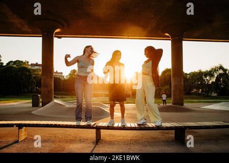 Bonne adolescente dansant sur le banc tout en appréciant sous le pont pendant le coucher du soleil Banque D'Images