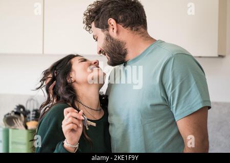 Un jeune couple marié se réjouit de l'achat de la nouvelle maison - les deux jeunes mariés regardent dans les yeux de l'autre et tiennent les clés de la maison Banque D'Images