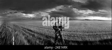 Paysage avec un chasseur de gibier sur les hautes terres transportant un fusil de chasse pour les oiseaux dans le comté rural de Stark, Dakota du Nord, lors d'une journée venteuse de tempête. Banque D'Images