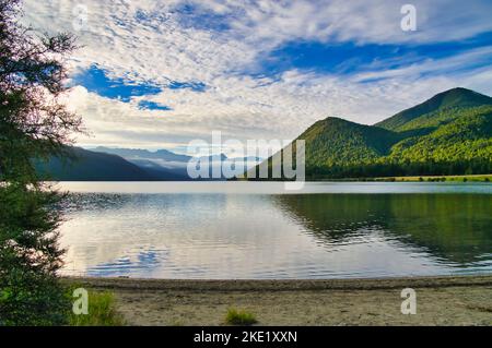 Lac Rotoroa, parc national Nelson Lakes, Nouvelle-Zélande, un matin d'été. Soleil bas éclairant les montagnes vertes et la brume pendant dans la vallée Banque D'Images