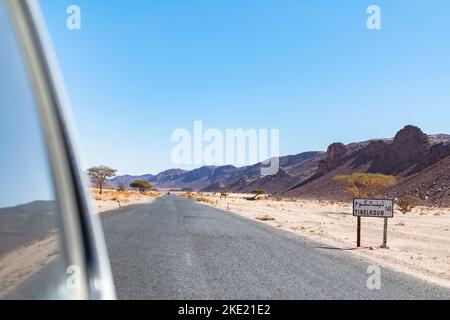 Tin El Koum, Algérie. Vue de la fenêtre arrière de voiture 4X4 Tinelkoum Desert Road plaque avec un dromadaire sur le reg, les montagnes Rocheuses et le ciel bleu. Banque D'Images
