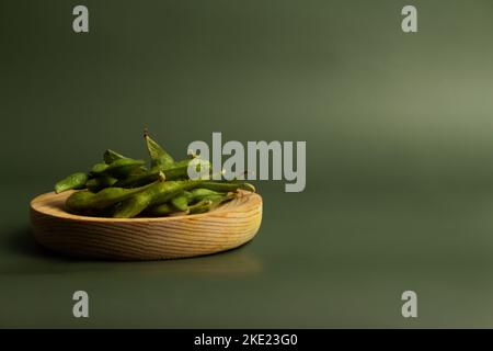 assiette en bois avec gousses de soja sur fond vert lisse et espace de copie Banque D'Images