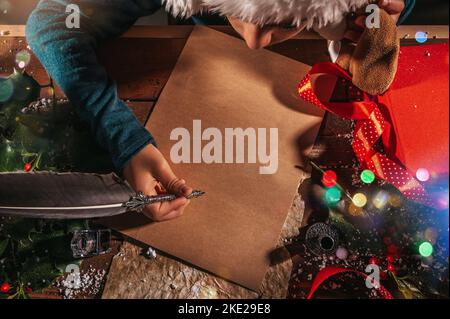 Un enfant avec un chapeau de noël écrit une lettre au père noël pour des cadeaux Banque D'Images