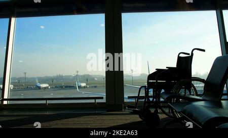 à l'aéroport, dans la salle d'attente, sur le fond de la fenêtre donnant sur l'avion et la piste, se trouve un fauteuil roulant, vous pouvez voir ses contours. Photo de haute qualité Banque D'Images